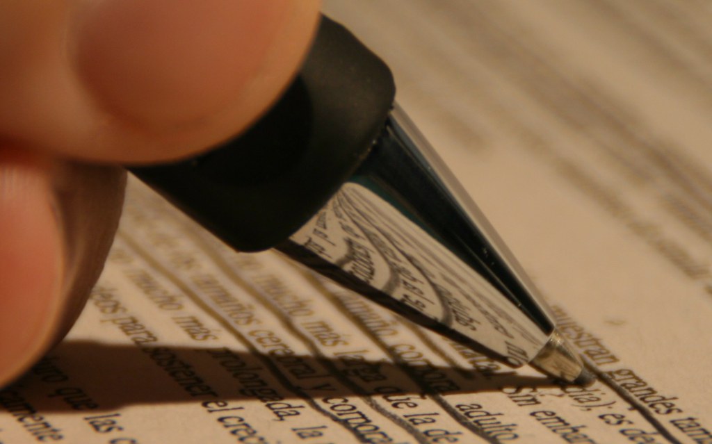 Close-up of a hand holding a black pen over printed text on paper.