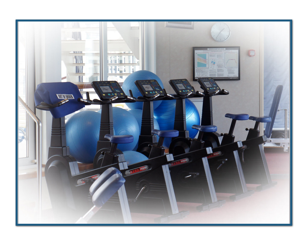 Row of stationary exercise bikes and blue exercise balls in an empty gym with windows behind