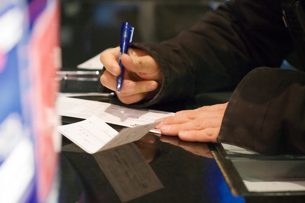 Close-up of hands, one holding a blue pen, over printed forms on a dark reflective counter